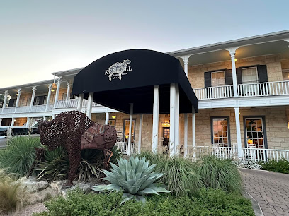 Exterior of the historic Kendall Inn with a black awning, limestone facade, and a rustic metal buffalo sculpture in the foreground. Kendall Inn Historic Hotel Entrance and Marquee